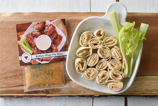 Buffalo wing dip mix, tortilla roll-ups with celery on a wooden board.