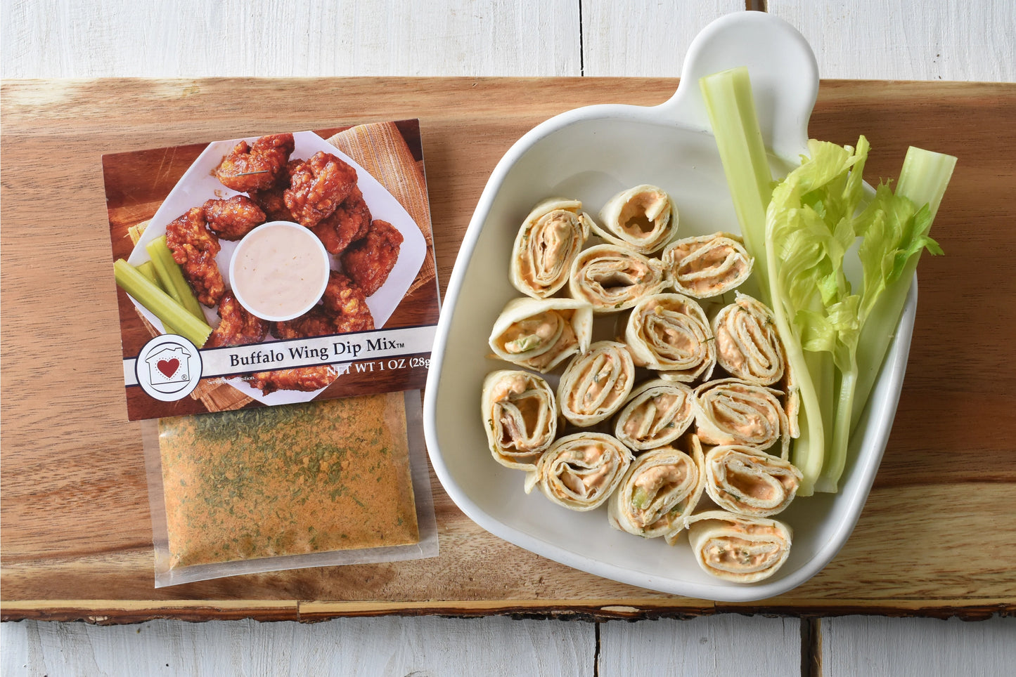 Buffalo wing dip mix, tortilla roll-ups with celery on a wooden board.