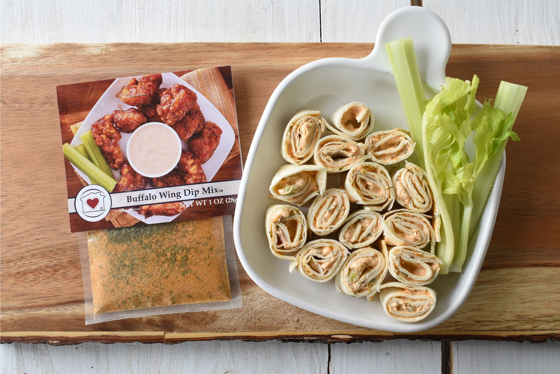 Buffalo wing dip mix, tortilla roll-ups with celery on a wooden board.